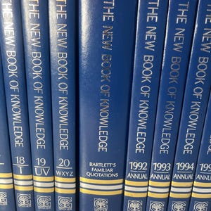 Może przedstawiać: Kolekcja niebieskich książek w twardej oprawie zatytułowanych "The New Book of Knowledge". Grzbiety mają złote litery i zawierają numery tom&oacute;w oraz tytuł "Bartlett's Familiar Quotations". Książki pochodzą od Grolier.