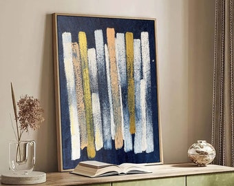 May include: A green cabinet with three doors and rounded edges sits on a wooden floor. A framed abstract painting with vertical brushstrokes in shades of blue, white, and yellow hangs above the cabinet. A book sits on top of the cabinet, and a small decorative object sits on the cabinet to the right of the painting.