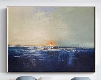 May include: Abstract painting of a seascape with a sunset over the ocean. The painting is done in shades of blue, green, and orange. It is framed in a gold frame and hanging on a white wall above a white couch.