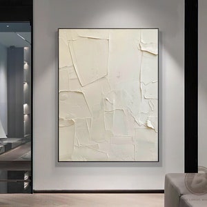 May include: Abstract white textured painting with a modern minimalist style. The painting is framed in a thin black frame and hangs on a white wall.