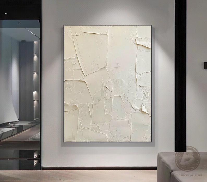 May include: Abstract white textured painting with a modern minimalist style. The painting is framed in a thin black frame and hangs on a white wall.