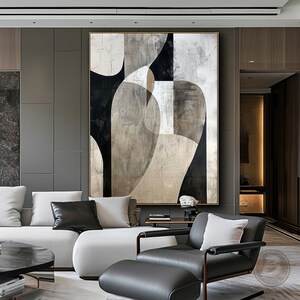 May include: Abstract art painting with black, white, and gray geometric shapes on a textured canvas. The painting is framed in a gold frame and hangs on a gray wall in a modern living room.