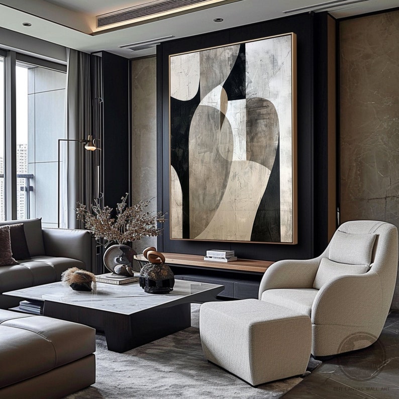 May include: A large abstract painting with black, white, and gray geometric shapes on a canvas. The painting is hanging on a wall in a modern living room with a gray couch, a coffee table, and a chair.