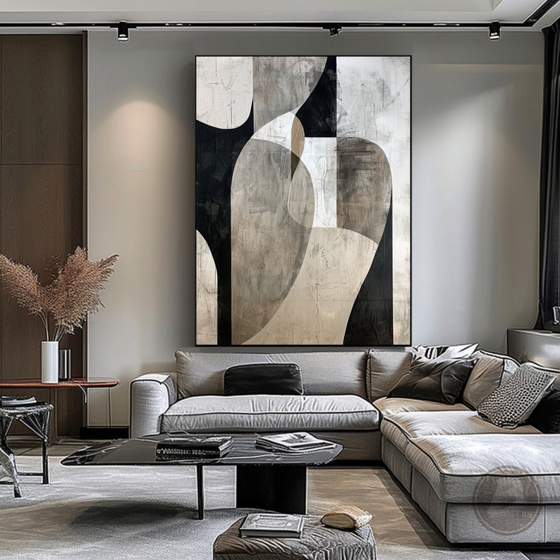 May include: Abstract art painting with black, white, and gray geometric shapes on a canvas. The painting is hanging on a wall in a living room with a gray sectional sofa and a black coffee table.