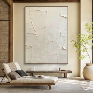 May include: A large, abstract painting with a white background and textured brushstrokes. The painting is framed in a thin, brown frame and is hanging on a wall in a modern living room.