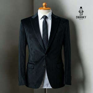 Peut inclure: Un blazer en velours vert foncé avec une fermeture à bouton unique et une cravate à motif noir. Le blazer a un revers cranté et une coupe ajustée.