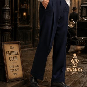 May include: Navy blue pleated trousers with a high waist, a black leather belt, and cuffed hems. The trousers feature a subtle embroidered logo on the upper thigh area. The garment is paired with black leather dress shoes and a white pinstriped shirt.