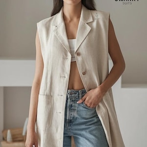 May include: A beige linen sleeveless vest with a notched collar and button fastening. The vest features two front pockets and a longline design. The model is wearing blue jeans. The logo "SWANKY SUITS" is visible in the upper right corner.