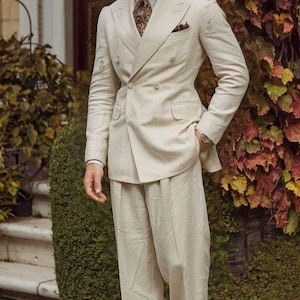 Könnte beinhalten: Ein cremefarbener zweireihiger Anzug mit hellblauem Hemd, gemusterter brauner Krawatte und Einstecktuch. Das Outfit umfasst einen cremefarbenen Fedora mit schwarzem Band und zweifarbige braun-cremefarbene Lederschuhe. Text: SWANKY SUITS.