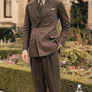 May include: A brown double-breasted suit with matching trousers and a brown hat. The suit has a white pocket square and a patterned tie. The image includes the text "SWANKY SUITS" and a logo. The suit is a classic style.