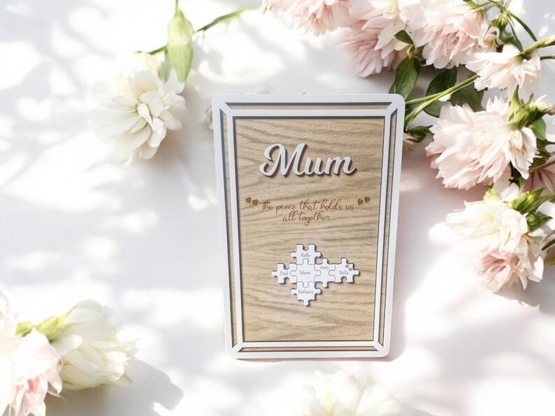 May include: Wooden framed plaque with the word "Mum" in cursive. The plaque has a light wood grain background and includes the text "the pieces that hold us all together". A puzzle piece design is at the bottom.