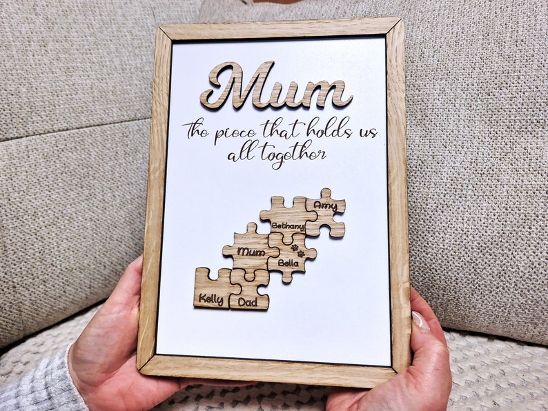 May include: Wooden framed sign with the word "Mum" in a cursive font. The text "the piece that holds us all together" is below. Puzzle pieces with names are below the text.