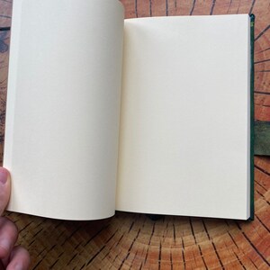 K&ouml;nnte beinhalten: Ein offenes, leeres Notizbuch mit einem dunkelgr&uuml;nen Einband. Das Notizbuch liegt auf einer Holzoberfl&auml;che.