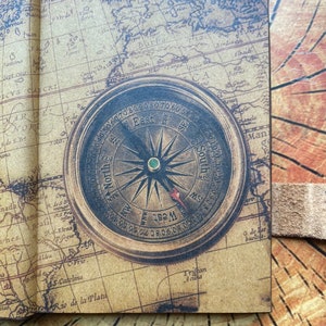 K&ouml;nnte beinhalten: Ein Kompass im Vintage-Stil mit braunem Lederbezug und einem Kartenhintergrund. Das Kompassgesicht ist mit den Himmelsrichtungen gekennzeichnet und hat eine goldfarbene Nadel.