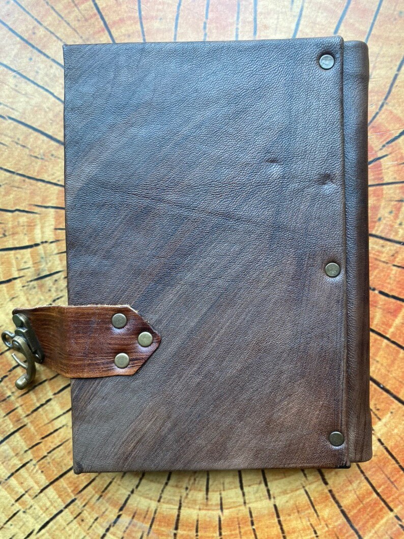 K&ouml;nnte beinhalten: Ein braunes, ledergebundenes Tagebuch mit einem braunen Lederriemen und einem Metallverschluss. Das Tagebuch hat einen abgenutzten Look und ist geschlossen.