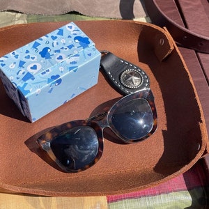 May include: A brown leather tray with a blue patterned box, sunglasses, and a silver key chain with a star design.