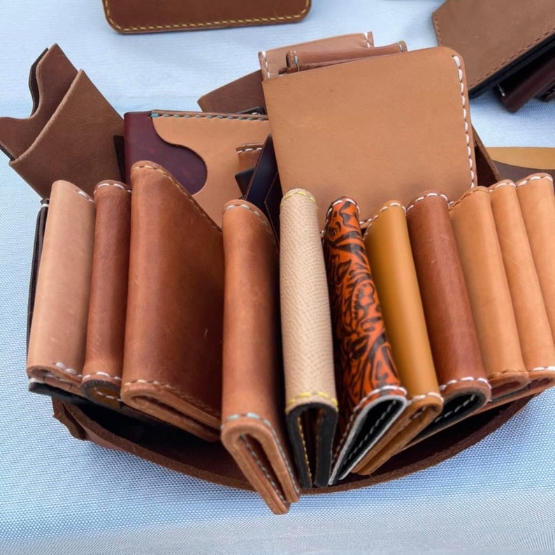 May include: A collection of brown leather wallets with different designs and stitching. The wallets are arranged in a fan shape and are displayed on a brown surface.