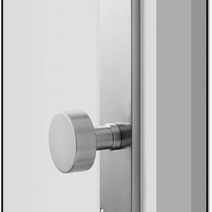 Może przedstawiać: Srebrny klamka do drzwi z okrągłym pokrętłem i prostokątną płytką. Klamka jest zamontowana na białych drzwiach.