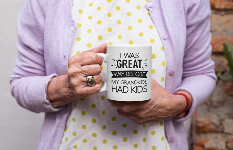 May include: White ceramic mug with black text that reads "I was great way before my grandkids had kids".