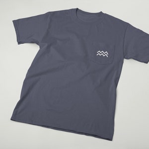 May include: A dark blue t-shirt with a white pocket featuring a stylized wave design.
