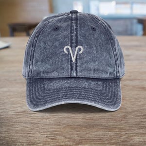 Op de afbeelding: Een blauwe denim baseballcap met een wit geborduurd sterrenbeeld Ram.