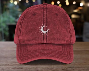May include: A red vintage washed cotton baseball cap with a white embroidered sun and moon design.