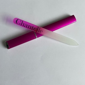 May include: A pink glass nail file with a white frosted surface and the word "Chantelle" printed on it. The file is in a pink case.