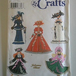 May include: Simplicity Crafts sewing pattern number 9062 for a doll dress. The pattern includes five different dress designs, including a red dress with a white trim, a green dress with a pink sash, and a black dress with a pink sash. The pattern is for one size.