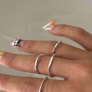 Può includere: Tre anelli d'argento su un dito. Gli anelli sono sottili e hanno un design semplice e curvo.