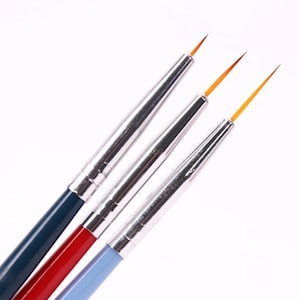 Peut inclure: Trois pinceaux à pointe fine avec des manches bleus, rouges et bleu clair. Les pinceaux ont des fûts en métal argenté et des pointes fines et pointues.