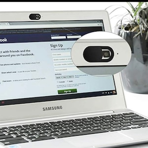 May include: A silver laptop computer with a black keyboard and a black webcam cover. The laptop is open and the screen shows a Facebook sign-up page. The laptop is sitting on a white surface.