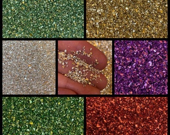 May include: Assortment of six colours of iridescent glitter, including green, gold, silver, purple, and red. The glitter is shown in small piles and in a hand.