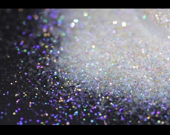 May include: A close-up of iridescent glitter, with a gradient from dark to light. The glitter is scattered on a black surface, with a white background.