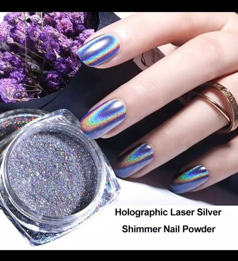 May include: A jar of holographic laser silver shimmer nail powder. The powder is a fine, glittery texture and is shown on a hand with nails painted with the powder.