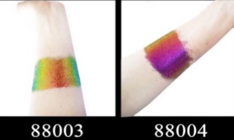 Op de afbeelding: Twee swatches van iriserende glitterpigment op de huid. De swatch links is regenboogkleurig, en de swatch rechts is paars. De swatches zijn gelabeld 88003 en 88004.
