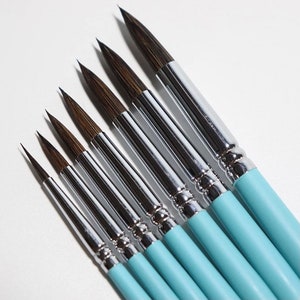 May include: Set of seven paint brushes with blue handles and silver ferrules. The brushes have different sizes and are arranged in a fan shape.