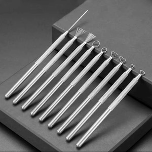 Puede incluir: Conjunto de nueve herramientas de escultura plateadas con puntas de diferentes formas. Las herramientas tienen un agarre texturizado y están dispuestas en una fila sobre una superficie gris.