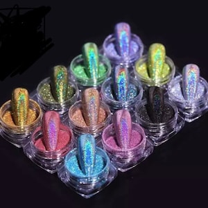 May include: A set of 12 small jars filled with iridescent glitter in various colors, including gold, green, blue, purple, and black. The jars are arranged in a grid pattern on a black surface.
