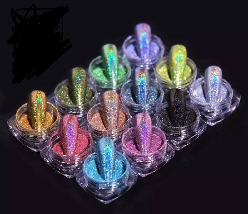 May include: A set of 12 small jars filled with iridescent glitter in various colors, including gold, green, blue, purple, and black. The jars are arranged in a grid pattern on a black surface.