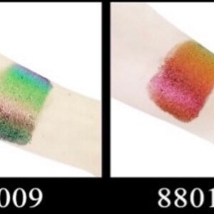 Op de afbeelding: Twee swatches van glinsterende oogschaduw op de arm van een persoon. De linker swatch is meerkleurig groen, blauw en bruin. De rechter swatch is rood, oranje en goudkleurig. De swatches zijn gelabeld met 88009 en 88010.