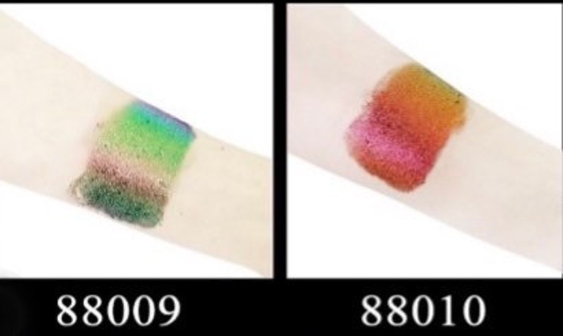 Op de afbeelding: Twee swatches van glinsterende oogschaduw op de arm van een persoon. De linker swatch is meerkleurig groen, blauw en bruin. De rechter swatch is rood, oranje en goudkleurig. De swatches zijn gelabeld met 88009 en 88010.