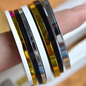 May include: Assortment of decorative trim tape rolls in gold, silver, black, and white. The tape is metallic and has a shiny finish.