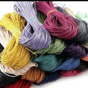 May include: A variety of colors of waxed cotton cord, including black, white, red, yellow, green, blue, purple, and brown. The cords are bundled together and are ready to be used for crafting projects.