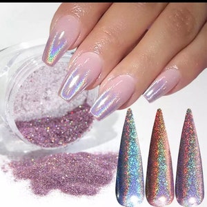 May include: A jar of iridescent glitter with a pink hue. The glitter is shown on a fingernail with a holographic finish.