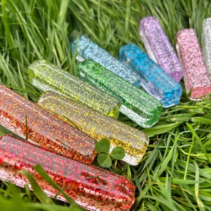 Puede incluir: Un arcoíris de piezas de vidrio rectangulares brillantes y coloridas dispuestas en semicírculo sobre un lecho de hierba verde.