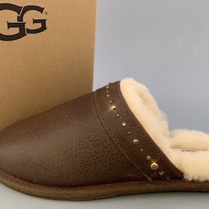 May include: Brown leather UGG slipper with a shearling lining and a decorative studded trim.