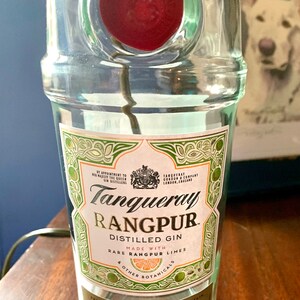 May include: A clear glass bottle of Tanqueray Rangpur distilled gin. The label is green and white with gold lettering and features a lime and the text "Made with Rare Rangpur Limes & Other Botanicals".