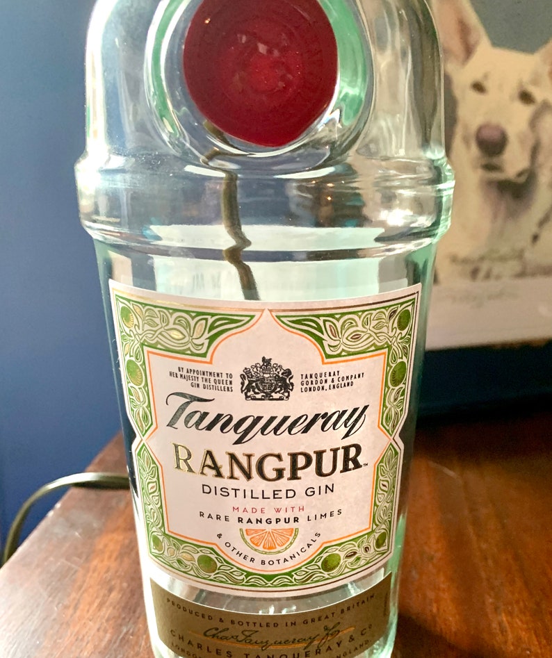 May include: A clear glass bottle of Tanqueray Rangpur distilled gin. The label is green and white with gold lettering and features a lime and the text "Made with Rare Rangpur Limes & Other Botanicals".
