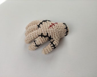 May include: A crocheted hand with black stitches and red embroidery. The hand is beige and has a stitched-up appearance.
