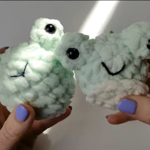 May include: Two crocheted plush toys in a light green color with black eyes. One toy has a simple smile and the other has a more detailed face with a stitched nose and mouth.